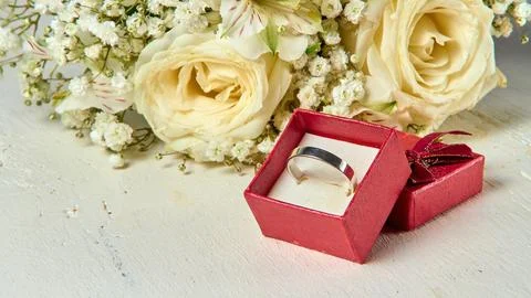 Silver ring in red gift box and bouquet of flowers on white textured wooden b Stock Photos