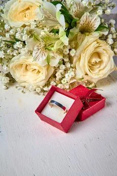 Silver ring in red gift box and bouquet of flowers on white textured wooden.. Stock Photos