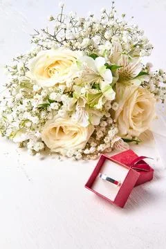 Silver ring in red gift box and bouquet of flowers on white textured wooden.. Stock Photos