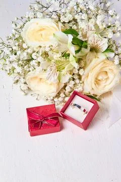 Silver ring in red gift box and bouquet of flowers on white textured wooden b Stock Photos
