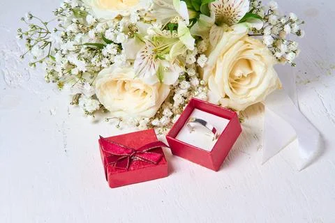 Silver ring in red gift box and bouquet of flowers on white textured wooden.. Stock Photos