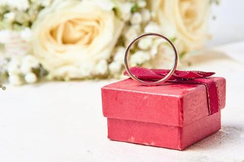 A silver ring stands on a red gift box and a bouquet of flowers on a white .. Stock Photos