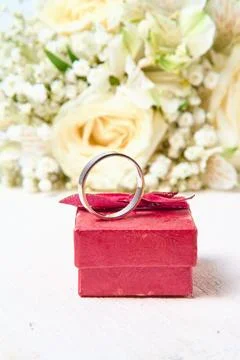 A silver ring stands on a red gift box and a bouquet of flowers on a white te Stock Photos