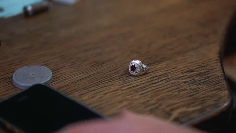Silver ring on a wooden table and the goldsmith takes a smartphone to call the Stock-Footage 73606960