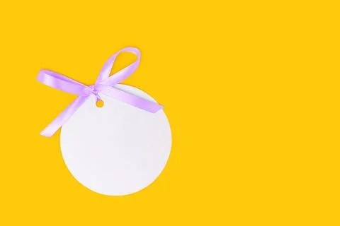 Silver round empty tag with tied blue ribbon bow on a yellow background. Stock Photos