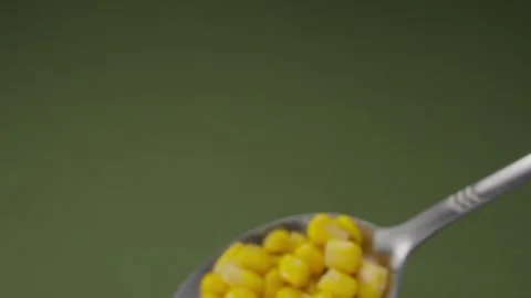 Silver spoon holding bright yellow sweet corn kernels on a green background. Stock Footage 285489057
