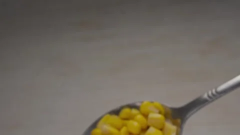 Silver spoon holding bright yellow sweet corn kernels on a grey background. Stock Footage 288044512