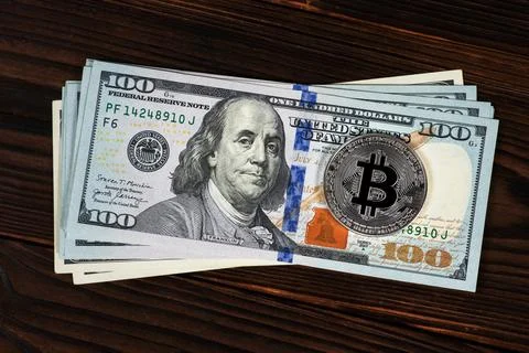 Silver symbolic coin Bitcoin on stack banknotes of one hundred dollars on woo Stock Photos