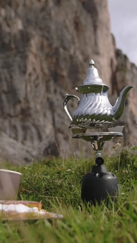 Silver teapot and cups on grass with dramatic rock wall of Dolomites in Stockbeeldmateriaal 318642813