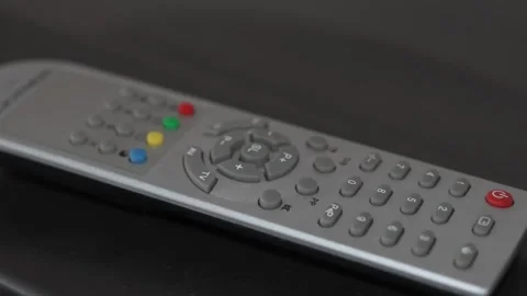 Silver television remote control with colorful buttons on dark surface Stock Footage 332982251