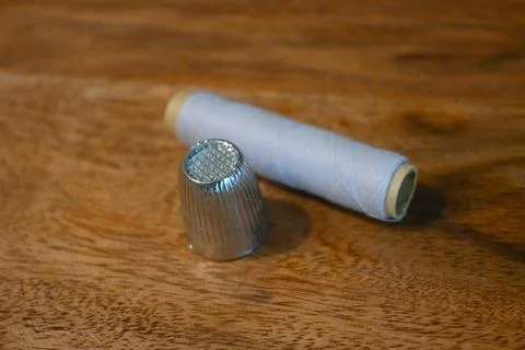 Silver thimble and blue thread spool on a wooden table Stock Photos