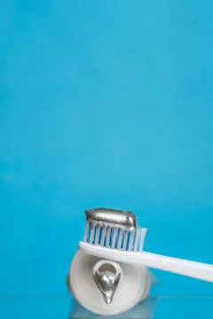 Silver toothpaste and toothbrush on blue backdrop.Сonceptual cosmetic background Stock Photos