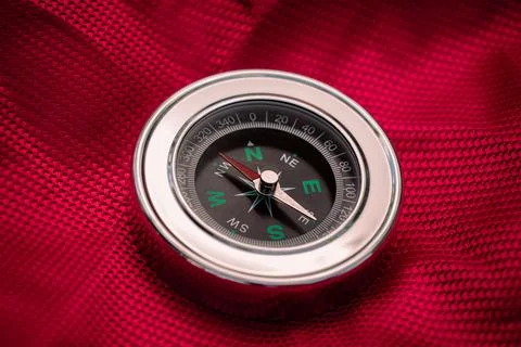 Silver traditional compass with arrow on red background Stock Photos