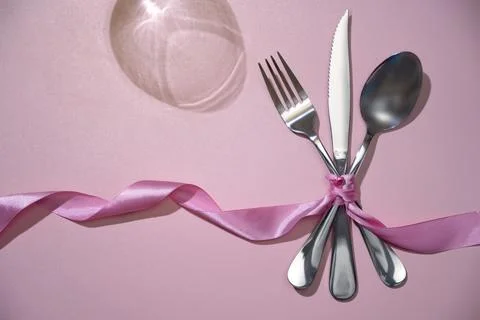 Silverware of fork, knife, and spoon tied up on pink ribbon Stock Photos