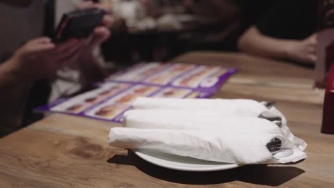 Silverware wrapped in white paper napkins on a plate at a restaurant table... Stock Footage 341783299