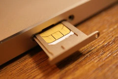 SIM card inserted into a mobile phone tray component on a wooden surface re.. Stock Photos