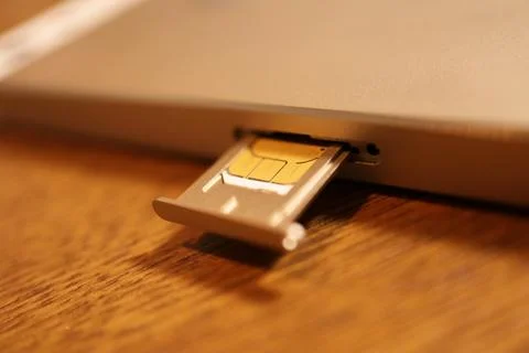 SIM card inserted into a mobile smartphone device tray on a wooden surface .. Stock Photos