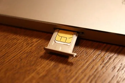 SIM card inserted into a mobile smartphone device tray on a wooden surface .. Stock Photos