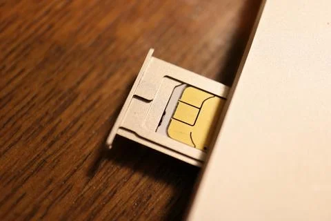 SIM card inserted in a smartphone tray slot on a wooden table surface shot .. Stock Photos