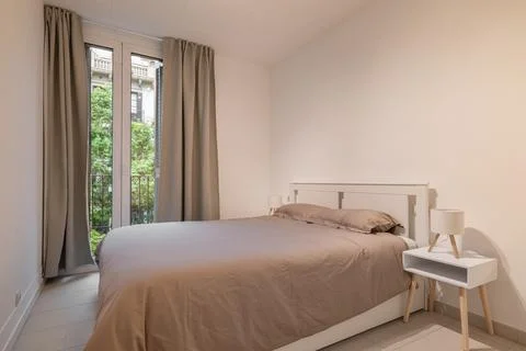 Simple bedroom interior with double bed, taupe bedding and large window with Фото