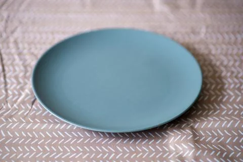 Simple blue plate on patterned tablecloth for minimalist home decor Stock Photos