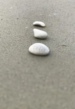 Simple closeup view of vertically arranged three white stones on grey sandy beac Stock Photos