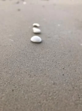 Simple closeup view of vertically arranged three white stones on grey sandy beac Stock Photos