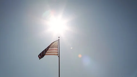A simple composition of an American flag flying backlit with a sunburst. 動画素材 115333444