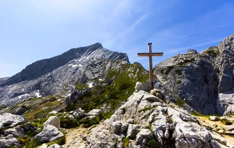 A simple cross on the rocks with a mountain range on a beautiful summer sunny Stock Photos