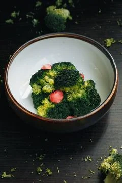 Simple dish: broccoli with garnish in earthenware bowl, dark textured surface Stock Photos