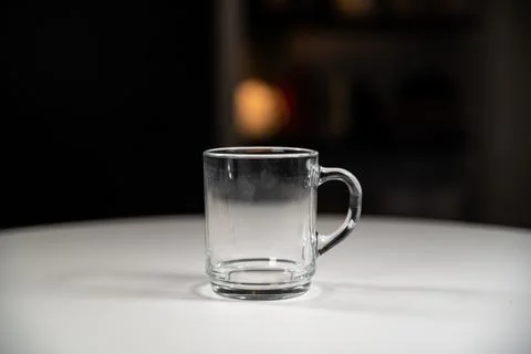 Simple elegant close up clear glass mug on a white table with a dark blurred Stock Photos