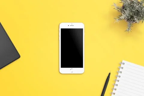 Simple, flat scene with white smart phone on yellow desk. Blank screen for ap Stock Photos