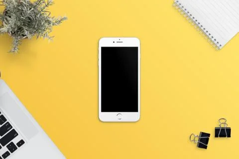 Simple, flat scene with white smart phone on yellow desk. Blank screen for ap Stock Photos