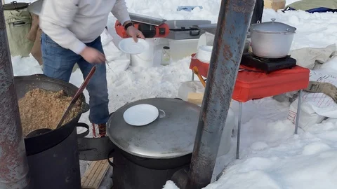 Simple meal. The cook puts buckwheat porridge on plates from a large cauldron. Video stock 124998028