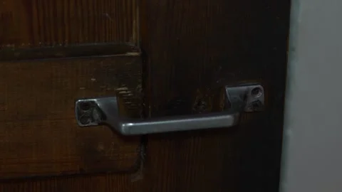 Simple metal door handle attached to a dark wooden door Stock Footage 332982566