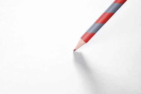 A simple red-gray pencil with a shadow on a piece of white paper. Stock Photos