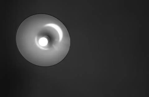 A simple round ceiling light glows against a dark, plain ceiling. Positioned  Foto stock