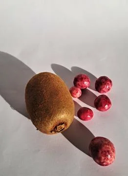 Simple snack composition combining fresh kiwi fruit and sweet candy dragees. Stock Photos