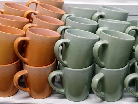 Simple solid orange and green ceramic cups displayed on supermarket shelves.. Stock Photos