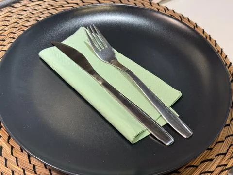 A simple table setting with a black plate green napkin fork and knife on a wo Stock Photos