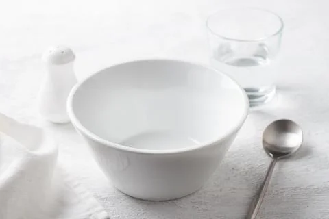 Simple table setting with white bowl, salt shaker, glass of water, and napkin on Stock Photos
