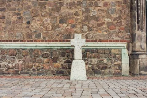 Simple white cross against rustic stone wall and paved ground Stock Photos