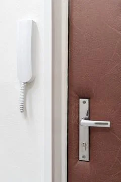 Simple white intercom or house phone attached to a wall next to a closed door Stock Photos