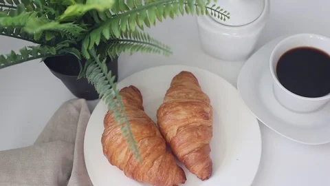 In a simple white plate, two delicious croissants. A cup of coffee stands next t Stock Footage 112103530