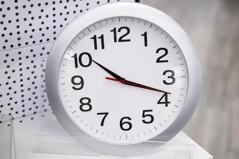 A simple white round wall clock stands and is sold on a shelf in a store Stock Photos
