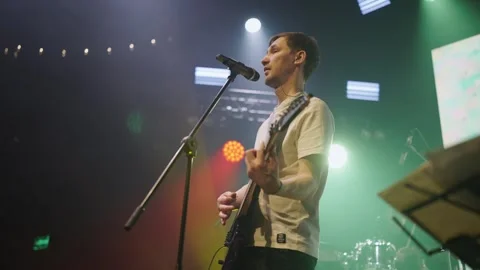 Singer with guitar performs on lighted stage. Guy singing into microphone close Stock Footage 243934731