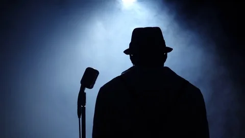 Singer at the microphone in smoke and white light sings. Black background Stock Footage 79614253