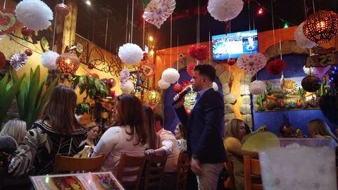 Singer Serenading Table In Mexican Restaurant With Latino Americans Eating F Stock Footage 127843284