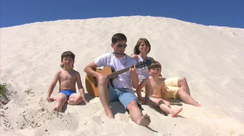 Singing family with guitar and harmonica sits on beach Stock Footage