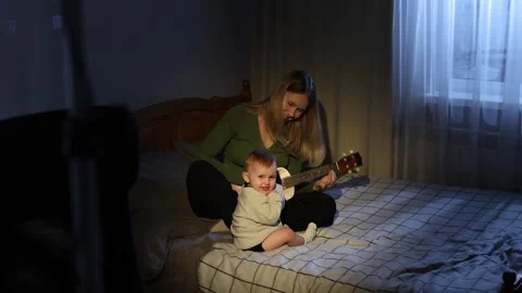 Singing a lullaby while playing the ukulele for a baby on a bed Stock Footage 303934364